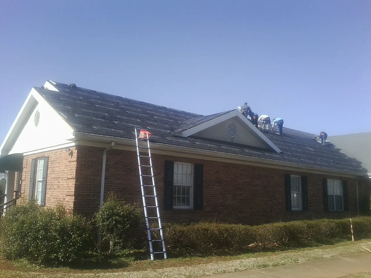 Crew tearing shingles off a brick ranch roof with a ladder set — Metal Roof Repair work by our crew in East Greenbush