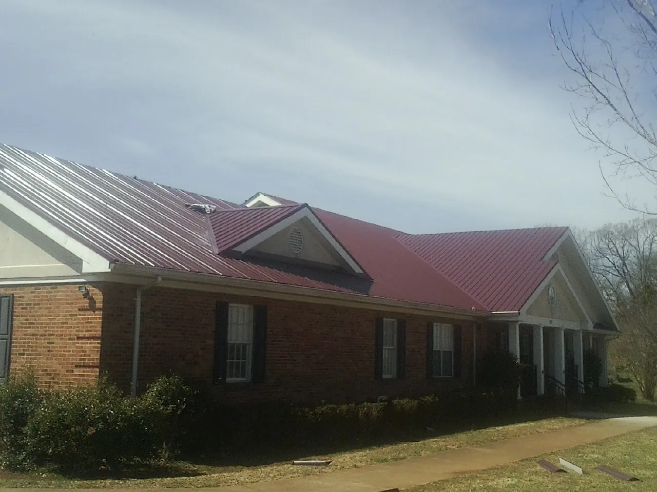 Red metal roof with gabled entries on a long brick building, from a Hail Damage Roof Repair job in East Greenbush
