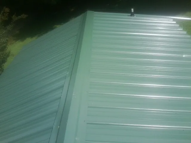New green metal panels meeting at the ridge of a roof — Flat Roof Repair work by our crew in East Greenbush
