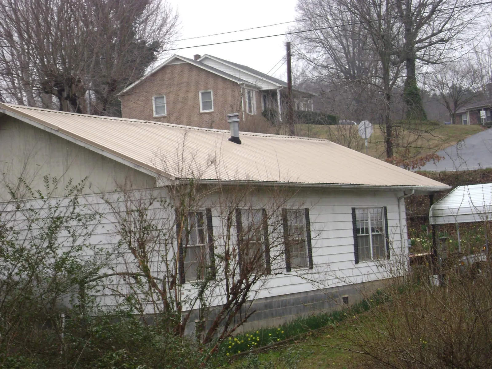 Tan metal roof on a white sided house set into a hillside — Commercial Roofing by Roofing Brothers in East Greenbush